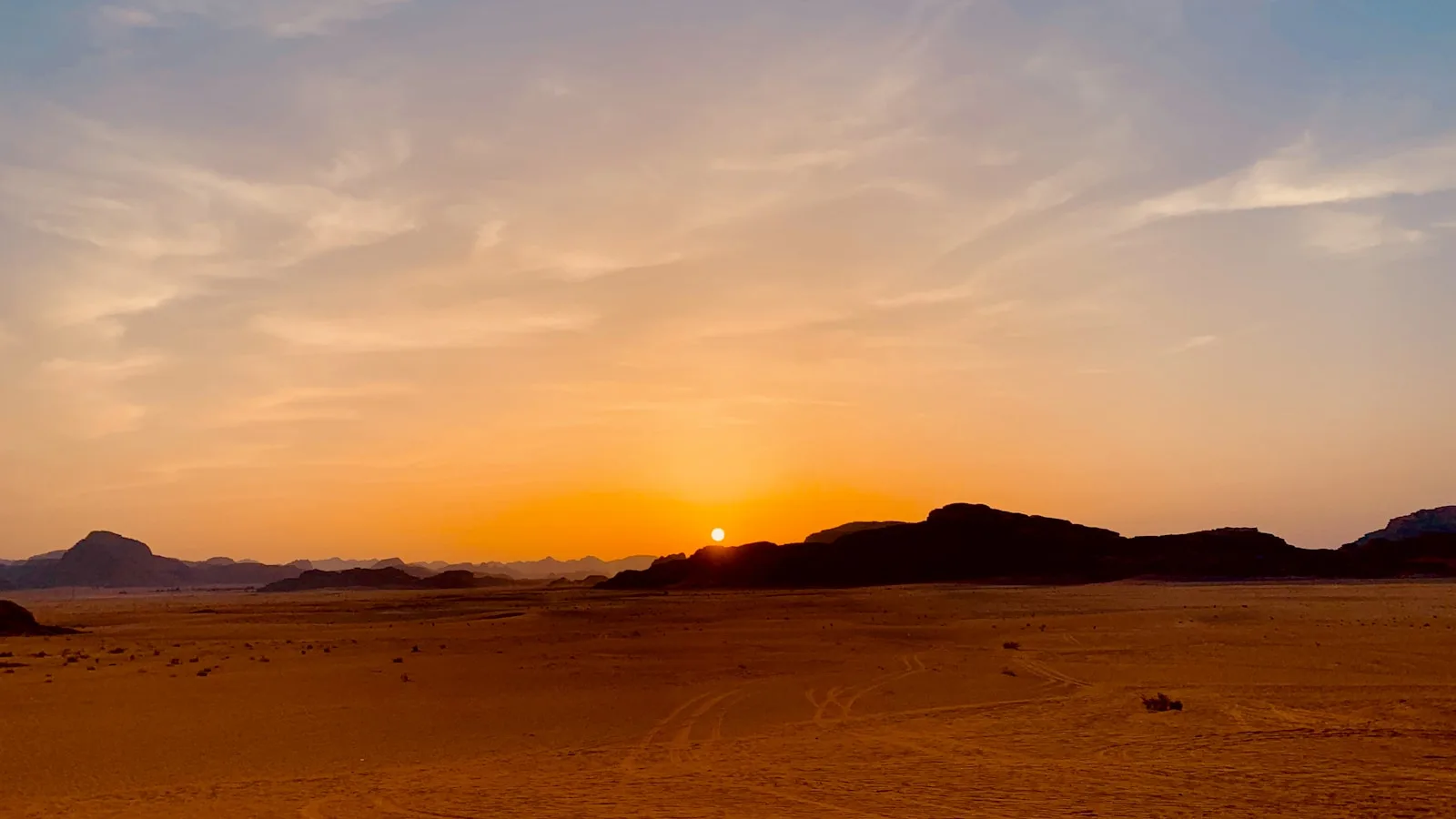 Voiture 4x4 sur une route désertique en Jordanie face à un coucher de soleil sur Wadi Rum